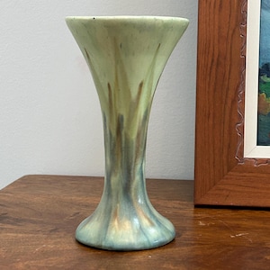 May include: A ceramic vase with a flared rim and a tapered body. The glaze features a blend of pale green, muted blue, and soft brown tones that transition vertically from the top to the base, creating a smooth, flowing colour gradient effect.