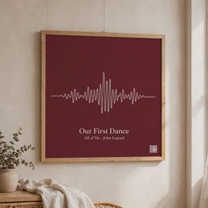 Peut inclure: Une affiche murale carrée dans un cadre en bois clair avec un fond bordeaux profond et un graphique d'onde sonore blanc horizontal. Le texte indique Our First Dance, All of Me - John Legend, avec un petit QR code blanc dans le coin.