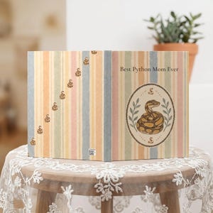 May include: A hardcover book with a pastel striped cover featuring a diagonal row of small snake illustrations on the left and a central oval frame on the right containing a coiled python illustration and the text Best Python Mom Ever.