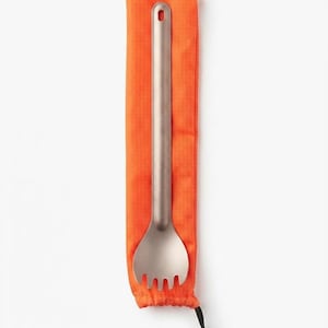May include: A metallic spork with a long handle and a hole at the top, resting on a bright orange fabric storage pouch. The pouch features a drawstring closure at the bottom with a black plastic toggle, providing a secure way to store the utensil.