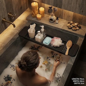 Può includere: Un vassoio rettangolare nero per vasca da bagno con superficie testurizzata, contenente una tazza bianca, un flacone con erogatore, un portasapone azzurro, una spugna da bagno rosa e una spazzola in legno. Misura 70 cm di lunghezza, 22 cm di larghezza e 3 cm di profondità.