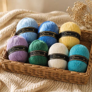 May include: Seven round balls of yarn in light blue, medium blue, yellow, purple, green, white, and turquoise. Each ball features a black paper band with the text Lamb baby printed in white, wrapped around the center of the yarn.