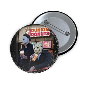 Peut inclure: Un badge rond avec une épingle au dos représentant deux personnages portant des masques de films d'horreur, l'un blanc et l'autre de hockey, tenant des gobelets Dunkin Donuts devant une devanture Dunkin Donuts avec le logo de la marque.