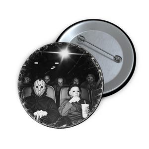 May include: A circular pin-back button featuring a black and white image of several horror movie characters sitting in a movie theater. The characters are wearing masks and holding popcorn and a drink cup, with a distressed, vintage-style texture.