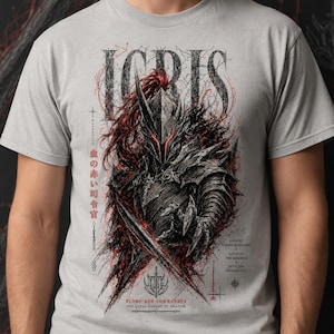 May include: A light gray t-shirt featuring a dark, detailed illustration of a knight in armor with red accents. The text reads "ICRIS", "BLOOD-RED COMMANDER", "THE LOYAL KNIGHT OF SHADOW", and Japanese characters. The design includes a sword and sharp lines.