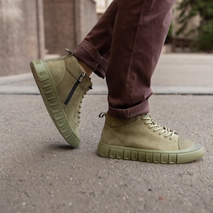 Può includere: Un paio di scarpe alte color verde oliva con tomaia in camoscio, suole in gomma abbinate con motivo a blocchi sul fianco, lacci tono su tono e chiusura laterale con zip nera. Il profilo laterale mette in risalto la suola strutturata.