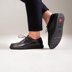 May include: A pair of black leather lace-up shoes with a moccasin-style toe seam. The shoes feature a thick, black rubber sole with a distinct tread pattern, a small red circular accent on the heel, and a blue label marked with the text DAVIS.