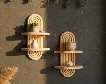 May include: Two light-coloured wooden wall shelves with a vertical arched design and two horizontal tiers each. The left shelf holds a small potted succulent and a white vase. The right shelf holds a stack of two small bowls and a glass candle holder.