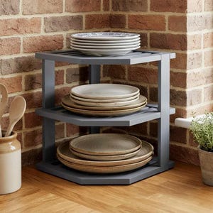May include: A three-tiered gray corner shelf unit constructed with a triangular frame. The top shelf holds a stack of white plates, the middle shelf holds a stack of light-colored plates, and the bottom shelf holds a stack of tan plates.