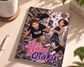 May include: A rectangular book titled Love is Hard for Otaku by Ale Fen, featuring an anime-style illustration of a man in a black hoodie, a woman in a beige cardigan, a black cat, and a black and white cat surrounded by stacks of books.