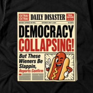 May include: A black t-shirt featuring a graphic of a newspaper titled Daily Disaster. The headline reads Democracy Collapsing! with a cartoon hot dog character giving a thumbs up. The text below says But These Wieners Be Slappin, Reports Confirm.