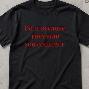 May include: A black short-sleeved t-shirt featuring the red text "Do it because, they said you couldn't." printed on the front. The shirt has a crew neckline and a standard fit, with the word "BLACK" visible in the top right corner.