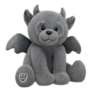 May include: A plush grey gargoyle toy with soft fur, small horns, and wings. The creature has black eyes, a stitched nose, and a smiling expression. A white paw pad on the right foot features the B-A-B logo in black text, indicating the brand.