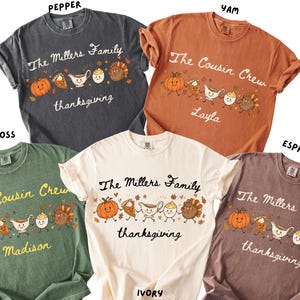 May include: Five short-sleeved crewneck t-shirts in charcoal, burnt orange, moss green, ivory, and brown. Each shirt features a graphic of cartoon Thanksgiving foods holding hands, with custom text like The Millers Family or The Cousin Crew.