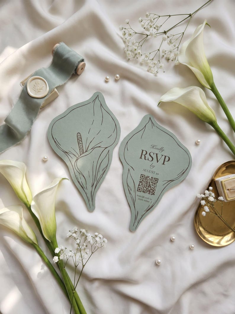 Puede incluir: Dos tarjetas de color verde salvia con forma de lirio de cala. Una presenta una ilustraci&oacute;n lineal de un lirio, la otra muestra el texto "Kindly RSVP by AUGUST 10" sobre un c&oacute;digo QR y la instrucci&oacute;n "Scan QR code to reply online".