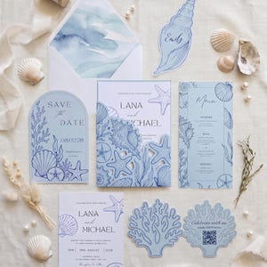May include: A wedding stationery suite featuring light blue and white paper goods with navy blue line art of seashells, starfish, and coral. Includes a save the date, invitation with a die-cut shell pocket, menu, and RSVP card with a QR code.