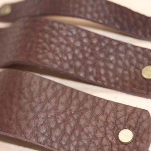 Op de afbeelding: Vier bruine lederen ladegrepen met messing accenten. Elke greep heeft een getextureerd oppervlak en een ronde messing knop.