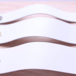 May include: Three white leather cabinet pulls with different colored metal accents. The pulls are curved and have a smooth finish.