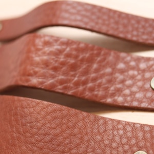 May include: Three brown leather straps with brass rivets. The straps are curved and have a textured surface.