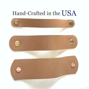 May include: Three brown leather drawer pulls with different metal hardware. The top pull has two gold metal knobs, the middle pull has two silver metal knobs, and the bottom pull has two copper metal knobs. Hand-Crafted in the USA.