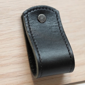 May include: Black leather drawer pull with a stitched edge and a silver metal screw.