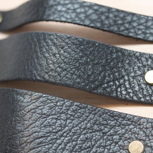 May include: Three black leather drawer pulls with gold metal accents. The pulls are stacked on top of each other.