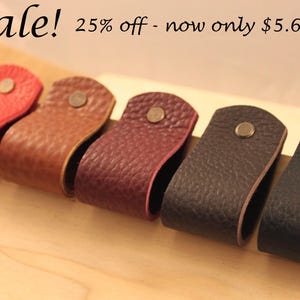 May include: Five leather drawer pulls in different colors: red, brown, burgundy, black, and dark gray. Each pull has a metal button in the center.