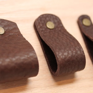 May include: Three brown leather drawer pulls with brass accents. Each pull has a loop shape and a single brass screw.