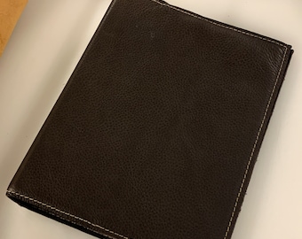Op de afbeelding: Een donkerbruin lederen notitieboek met een gestikte rand.