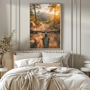 K&ouml;nnte beinhalten: Ein gerahmter Wandkunstdruck, der die Ich-Perspektive beim Fahren eines Mountainbikes auf einem Feldweg durch einen Wald in Richtung schneebedeckter Berge bei Sonnenuntergang zeigt, mit goldenem Licht durch die B&auml;ume und Bewegungsunsch&auml;rfe.