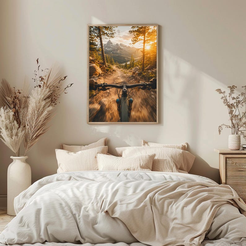 K&ouml;nnte beinhalten: Ein gerahmter Wandkunstdruck mit einer Ego-Perspektive eines Mountainbikes auf einem staubigen Pfad. Das Bild zeigt den Lenker im Vordergrund, hohe Kiefern und ferne Berggipfel, die in das goldene Licht eines Sonnenuntergangs getaucht sind.