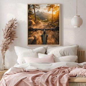K&ouml;nnte beinhalten: Ein gerahmter Wandkunstdruck mit einer Ego-Perspektive eines Mountainbikes auf einem Feldweg. Die Szene zeigt einen goldenen Sonnenuntergang &uuml;ber fernen Berggipfeln, mit hohen Kiefern entlang des Pfades und einer Bewegungsunsch&auml;rfe.