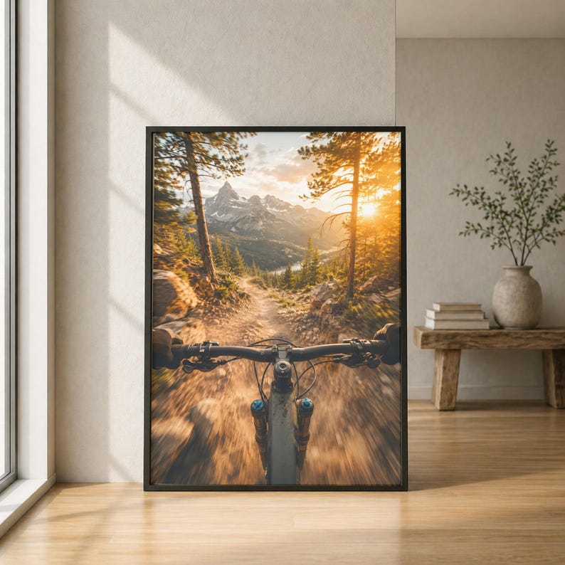 K&ouml;nnte beinhalten: Ein gerahmter Kunstdruck mit einer Ich-Perspektive beim Mountainbiken auf einem Waldweg. Die Szene zeigt einen hellen Sonnenuntergang &uuml;ber fernen schneebedeckten Bergen, umgeben von hohen Kiefern und einem dynamischen Bewegungseffekt.