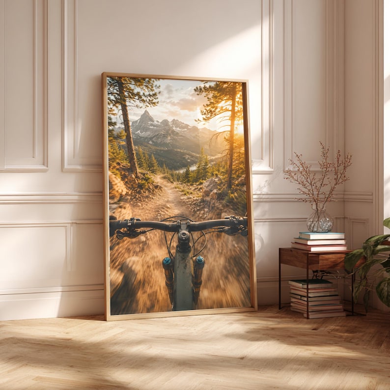 K&ouml;nnte beinhalten: Ein gerahmter Kunstdruck mit einer Ego-Perspektive eines Mountainbike-Lenkers auf einem Feldweg. Die Szene zeigt eine sonnendurchflutete Berglandschaft mit hohen Kiefern, felsigem Gel&auml;nde und einem entfernten Tal w&auml;hrend der goldenen Stunde.