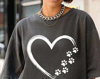 May include: A charcoal gray short-sleeved t-shirt featuring a large white heart outline on the chest. The right side of the heart is composed of a series of small white paw prints that trail upwards, creating a graphic design on the front of the garment.