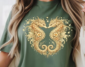 May include: An olive green t-shirt featuring a central graphic of two golden seahorses facing each other, their bodies and tails curving to form a heart shape. The seahorses are adorned with intricate floral details and small golden accents.