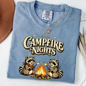 Retro illustration of two raccoons wearing bandanas roasting marshmallows over a campfire with the text Campfire Nights above them on a cream background. — product photo 12