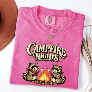 Retro illustration of two raccoons wearing bandanas roasting marshmallows over a campfire with the text Campfire Nights above them on a cream background. — product photo 5