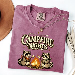 Retro illustration of two raccoons wearing bandanas roasting marshmallows over a campfire with the text Campfire Nights above them on a cream background. — product photo 16