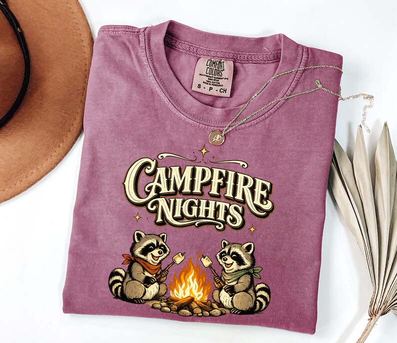 Retro illustration of two raccoons wearing bandanas roasting marshmallows over a campfire with the text Campfire Nights above them on a cream background. — product photo 16