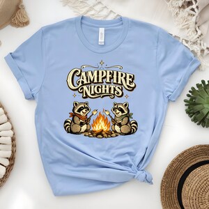 Retro illustration of two raccoons wearing bandanas roasting marshmallows over a campfire with the text Campfire Nights above them on a cream background. — product photo 6