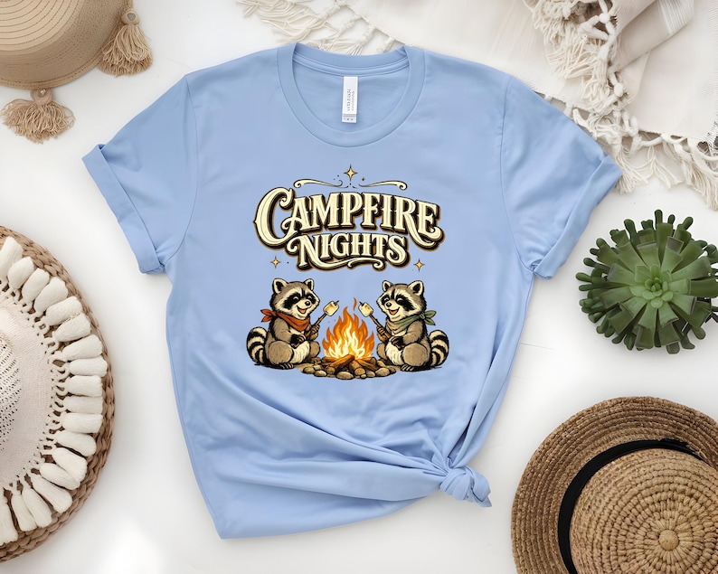 Retro illustration of two raccoons wearing bandanas roasting marshmallows over a campfire with the text Campfire Nights above them on a cream background. — product photo 6