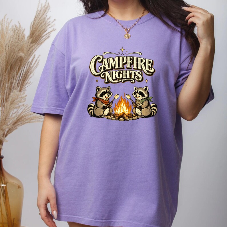 Retro illustration of two raccoons wearing bandanas roasting marshmallows over a campfire with the text Campfire Nights above them on a cream background. — product photo 3