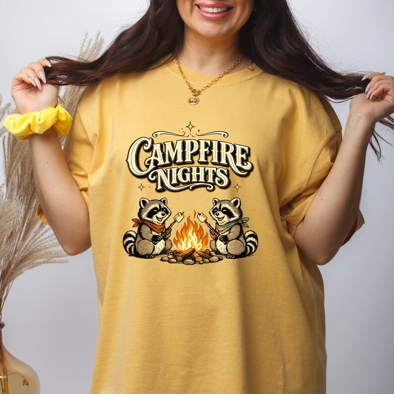 Retro illustration of two raccoons wearing bandanas roasting marshmallows over a campfire with the text Campfire Nights above them on a cream background. — product photo 9