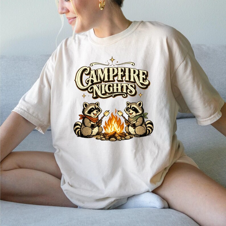 Retro illustration of two raccoons wearing bandanas roasting marshmallows over a campfire with the text Campfire Nights above them on a cream background. — product photo 4