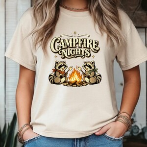 Retro illustration of two raccoons wearing bandanas roasting marshmallows over a campfire with the text Campfire Nights above them on a cream background. — product photo 7
