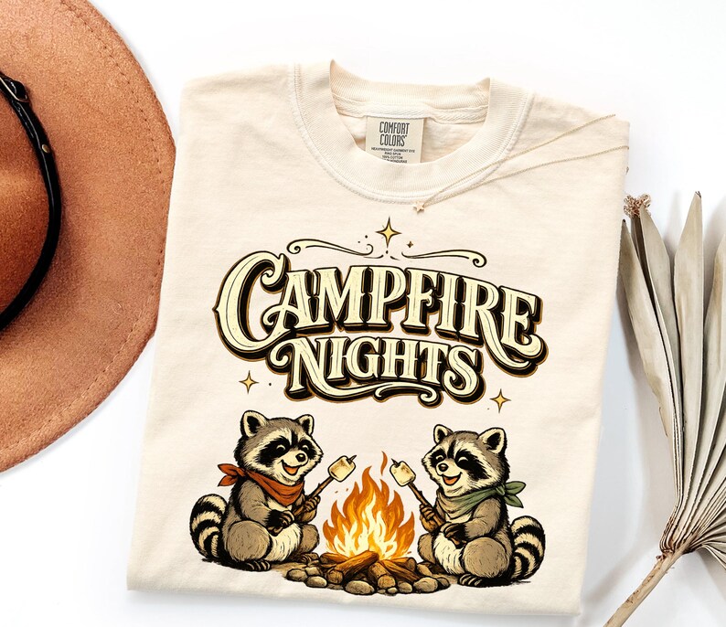 Retro illustration of two raccoons wearing bandanas roasting marshmallows over a campfire with the text Campfire Nights above them on a cream background. — product photo 14