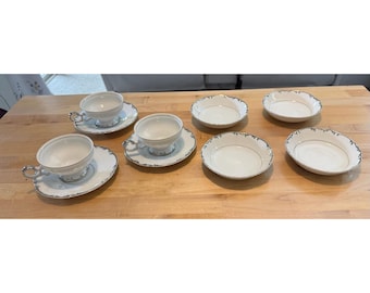 Może przedstawiać: Zestaw białej porcelanowej zastawy stołowej składający się z dwóch filiżanek do herbaty z pasującymi spodkami oraz czterech małych miseczek. Każdy element ozdobiony jest delikatnym srebrnym wzorem kwiatowym na falistych brzegach.