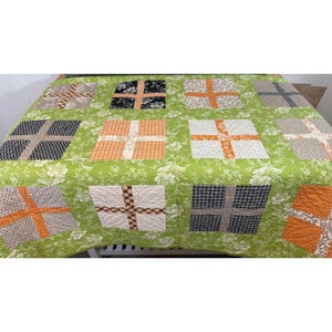 May include: A quilt featuring a bright lime green background with a white floral pattern. The quilt is composed of square blocks, each containing a cross shape made of various fabrics in orange, black, white, and grey with houndstooth and chevron prints.