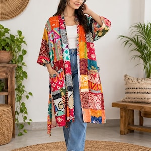 May include: A long-sleeved, open-front duster coat featuring a vibrant patchwork design with various colorful fabric squares in shades of red, orange, yellow, and blue. The garment includes two front pockets and is worn over a white top and blue jeans.